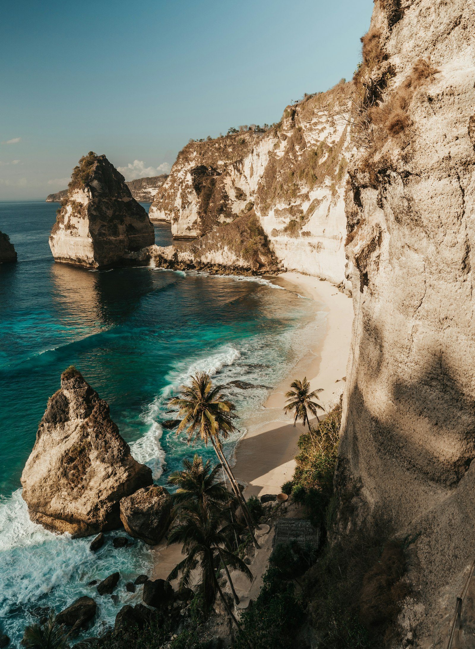 Limestone cliffs and a turquoise cove with palm trees in the Nusa islands